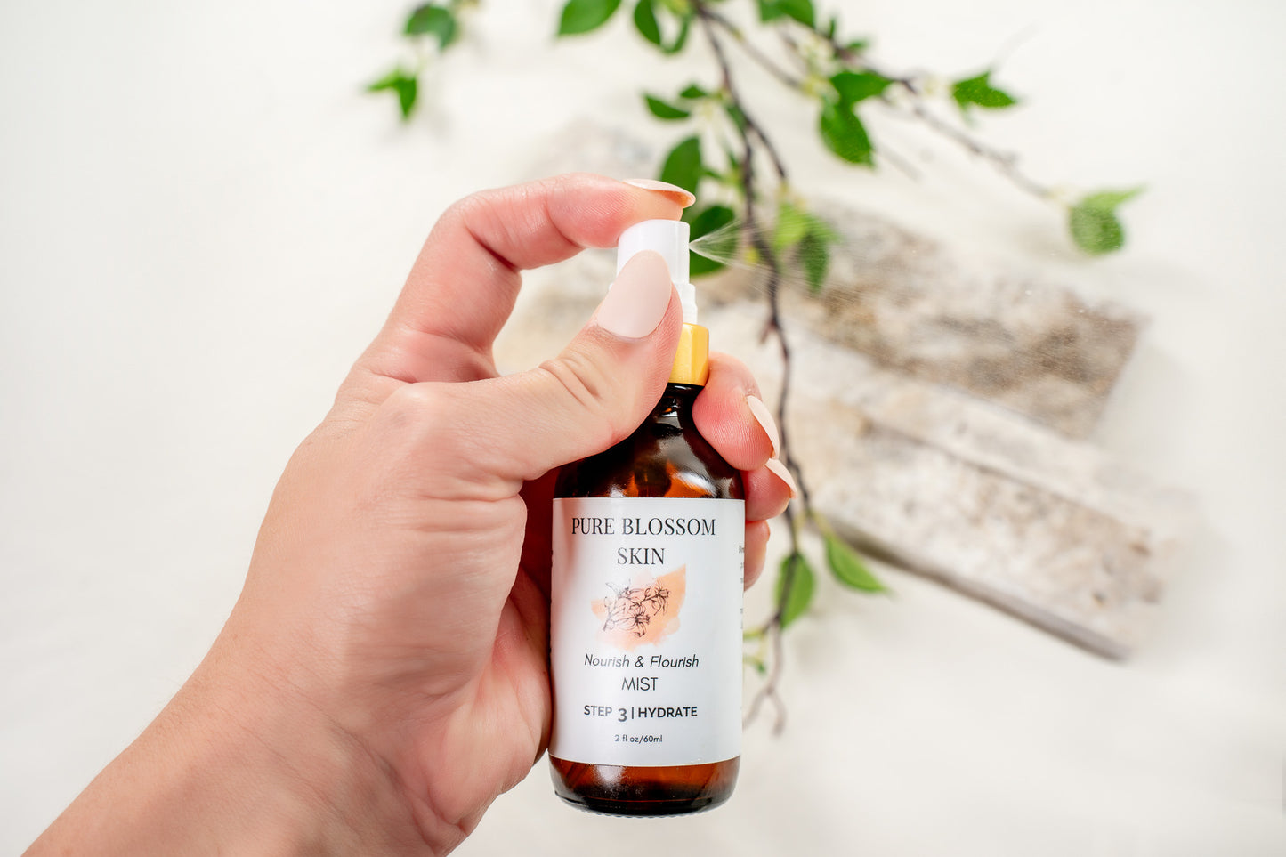Close up of hand holding 2oz amber glass spray bottle w/matte gold trim spraying Nourish & Flourish MIST | Pure Blossom Skin