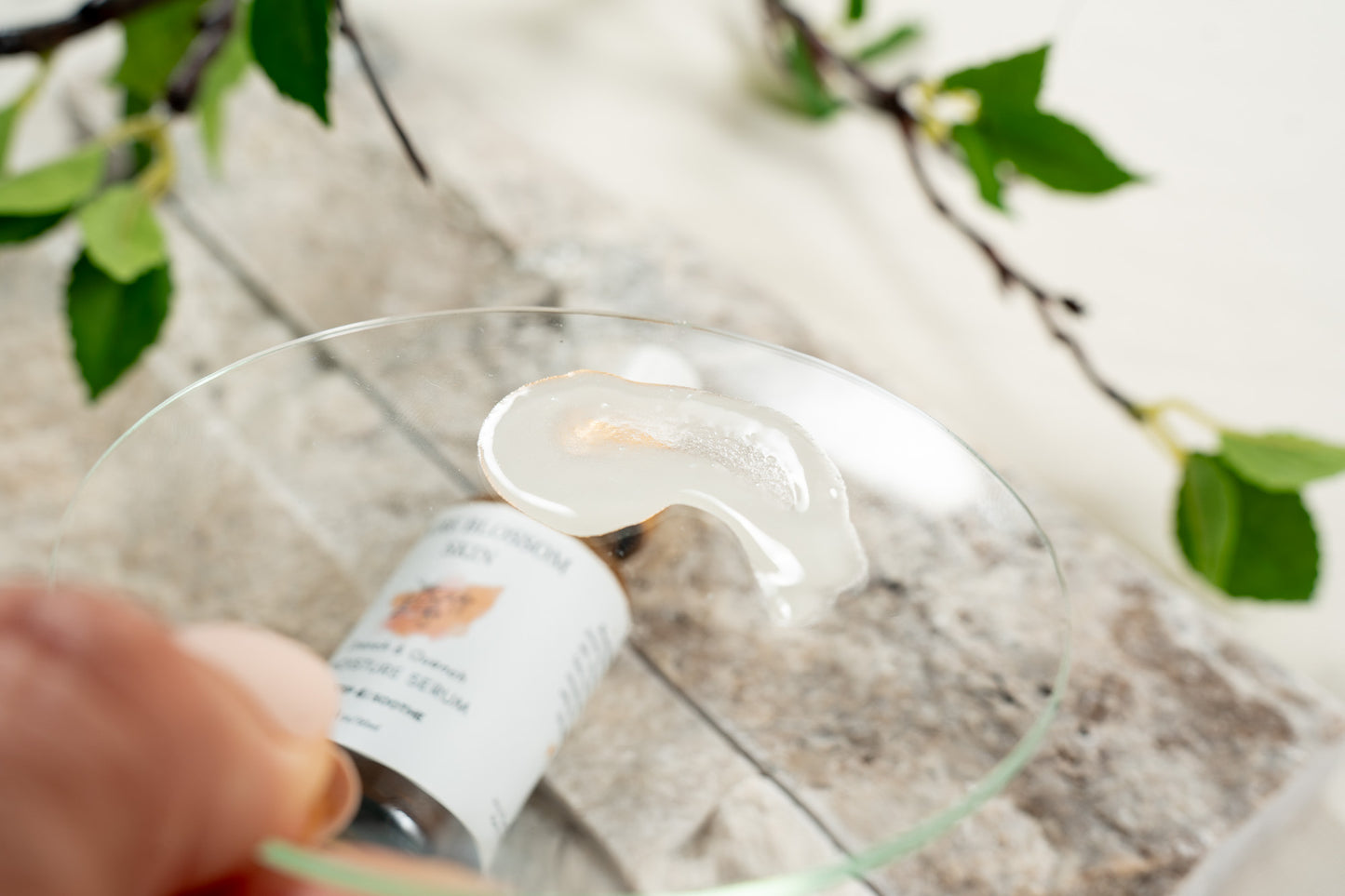Close up of glass disc with dollop of milky serum on it. 1oz amber glass bottle of Drench & Quench MOISTURE SERUM seen through the glass | Pure Blossom Skin