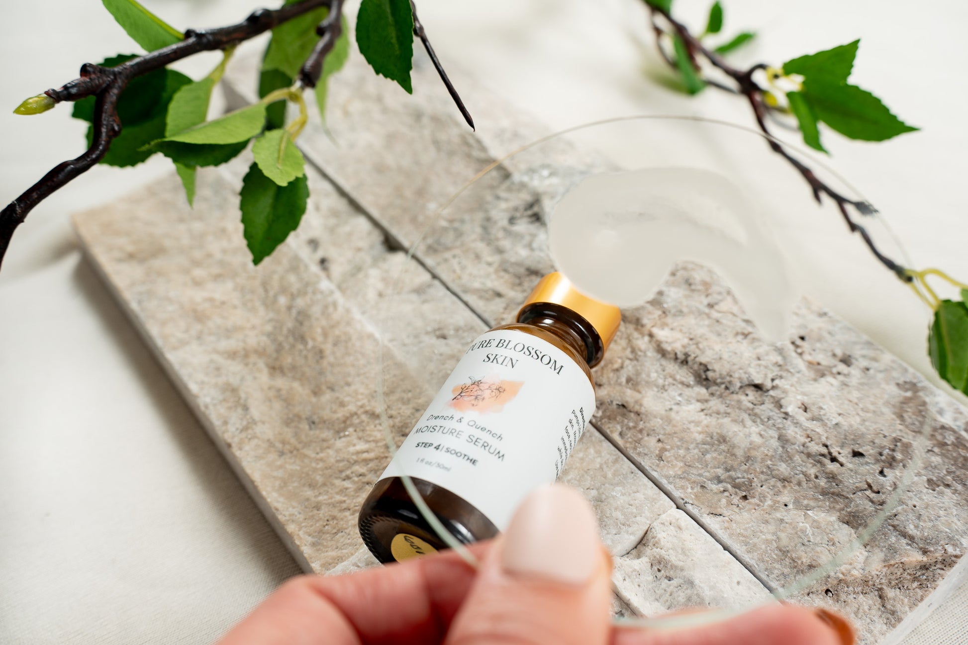 Close up of glass disc with dollop of milky serum on it. Clear view of 1oz amber glass bottle of Drench & Quench MOISTURE SERUM seen through the glass | Pure Blossom Skin